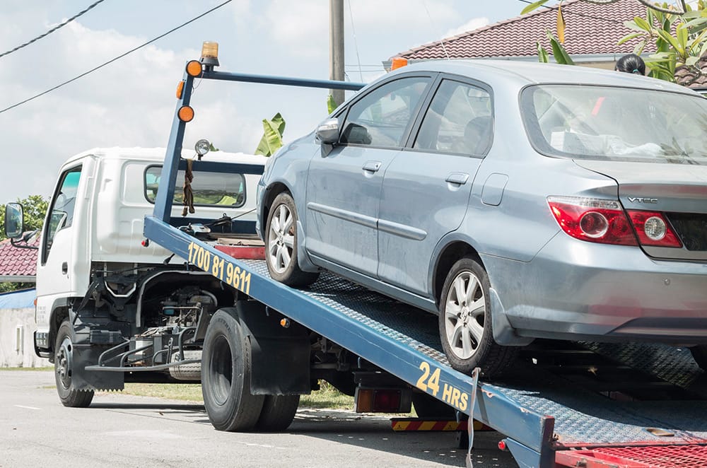A car being towed on a flatbed truck, indicating a towing service to avoid further issues.